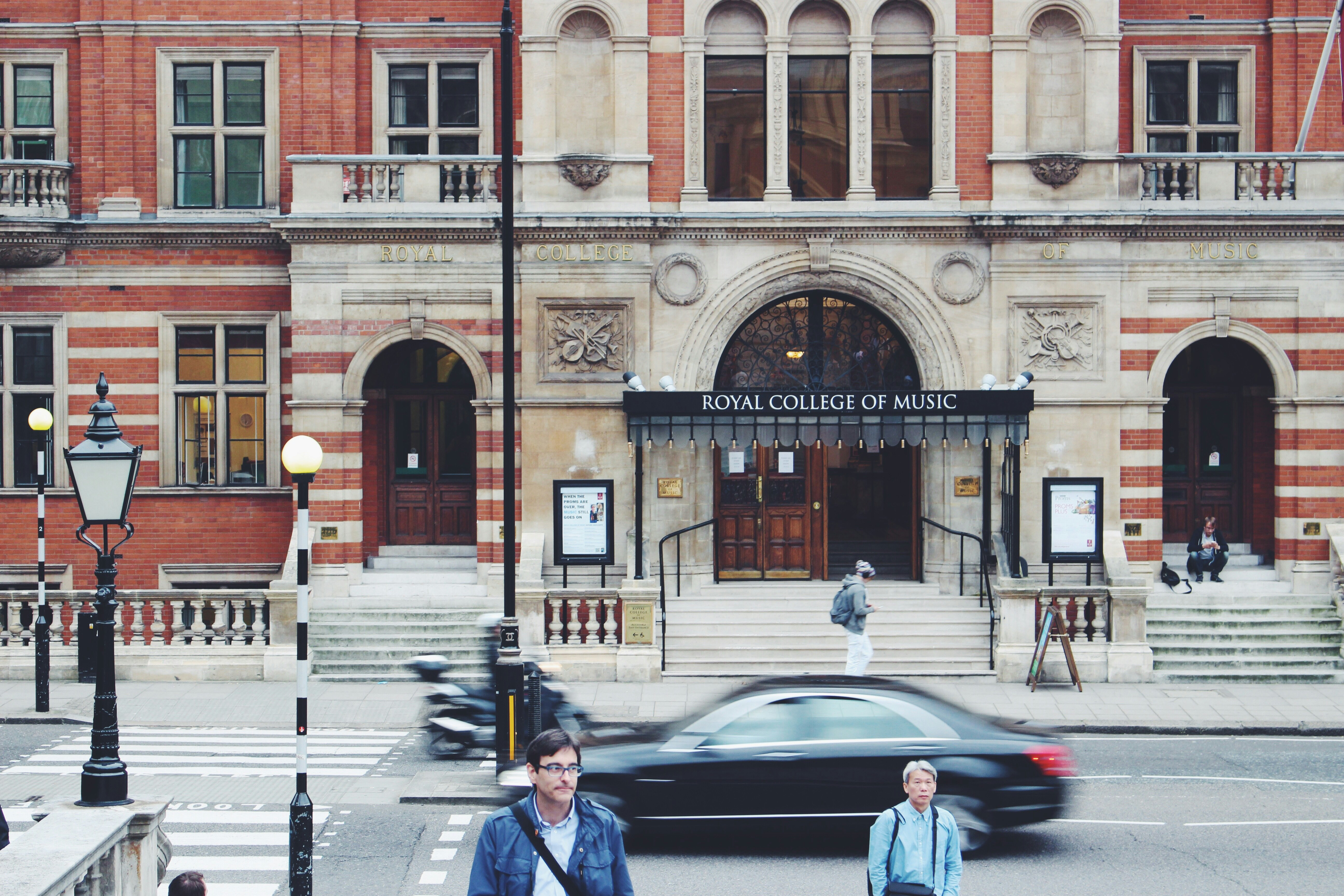 selective focus photography of man walking near Royal College of Music building